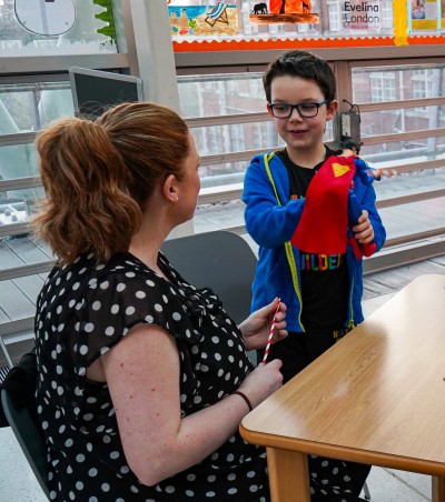 A boy is holding a Superman toy while his mum looks on