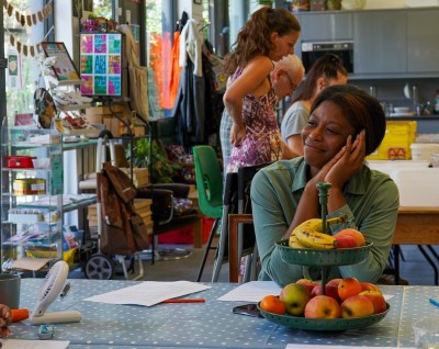 A Black woman sits at a table, looking to the side and smiling