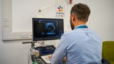 A man sits in a hospital room analysing an image on a computer screen