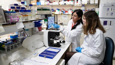 Two women wearing white lab coats are in a laboratory discussing some blood test results