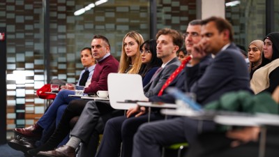 A group of people are sitting down at an event, looking towards a speaker