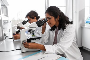 A scientist in a white lab coat looks into a microscope