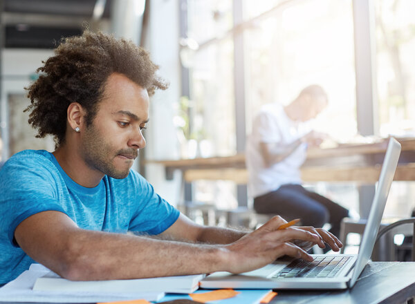 Stylish afro american student keyboarding on laptop computer while sitting at cafe table with textbooks  working on homework adobestock 158339583 overview