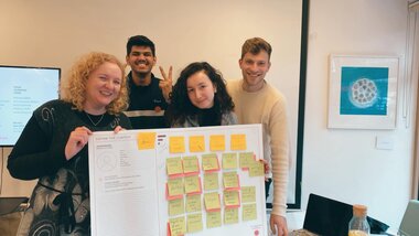 Jennie and colleagues holding a project board with - image taken at the Hackathon event